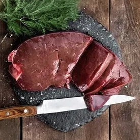 Ein großes, frisches Stück dunkle Rinderleber, fachgerecht in Scheiben geschnitten auf einer dunklen Schieferplatte präsentiert. Ein hochwertiges Naturprodukt der Metzgerei Walz, ideal für die frische Zubereitung mit Zwiebeln und Äpfeln.