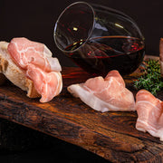 Dünn geschnittener Mainzer Schinken auf rustikalem Holzbrett mit Brot und einem Glas Rotwein – traditionelle Spezialität der Metzgerei Walz.