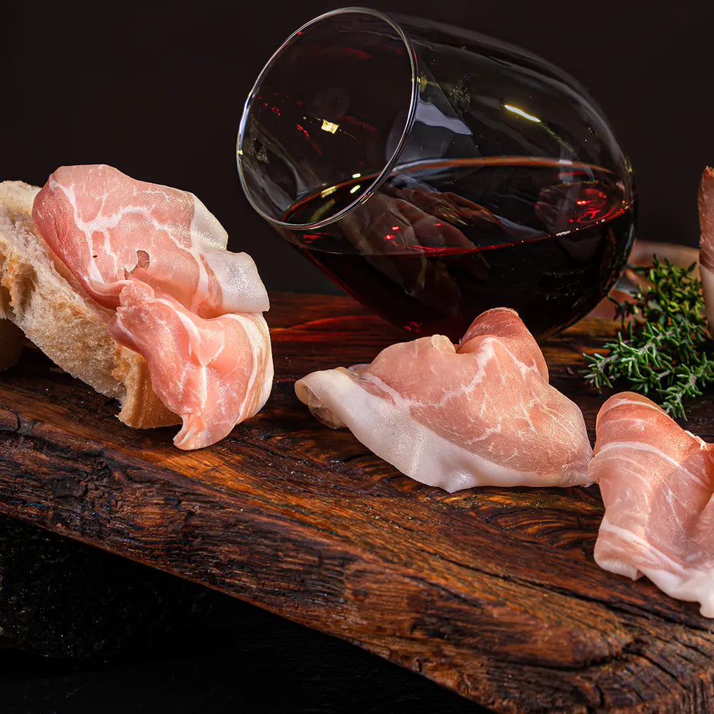 Dünn geschnittener Mainzer Schinken auf rustikalem Holzbrett mit Brot und einem Glas Rotwein – traditionelle Spezialität der Metzgerei Walz.