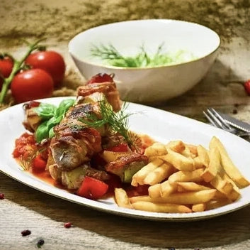 Herzhafte Schaschlik-Spieße in pikanter Tomatensoße, serviert mit knusprigen Pommes Frites auf einem weißen Teller. Das Fleisch ist perfekt gegrillt und wird durch die fruchtige Soße und frische Kräuter ideal abgerundet.